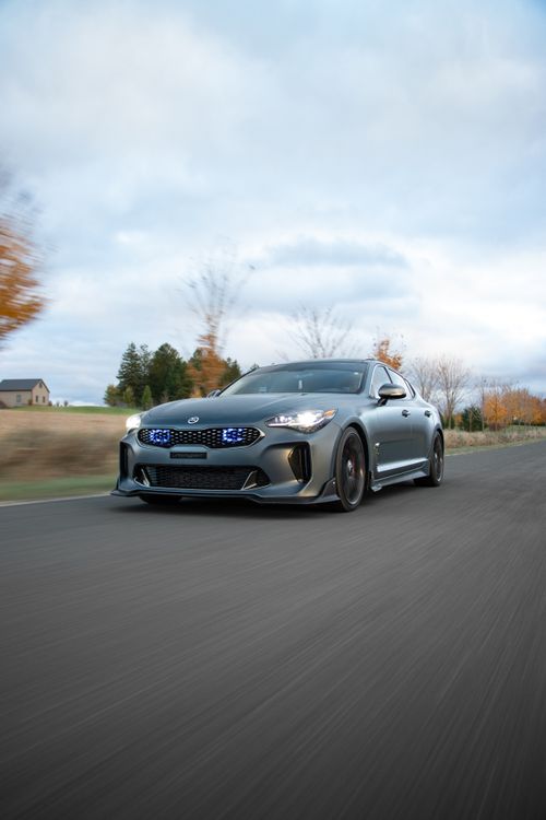 Free A sleek sports car speeds along a scenic road surrounded by autumn foliage. Stock Photo