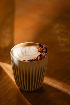 A beautifully crafted cafe latte with latte art and dried rose petals, captured in warm light.