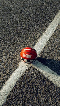 Close-up of a red basketball on a textured outdoor court, highlighting the sport.