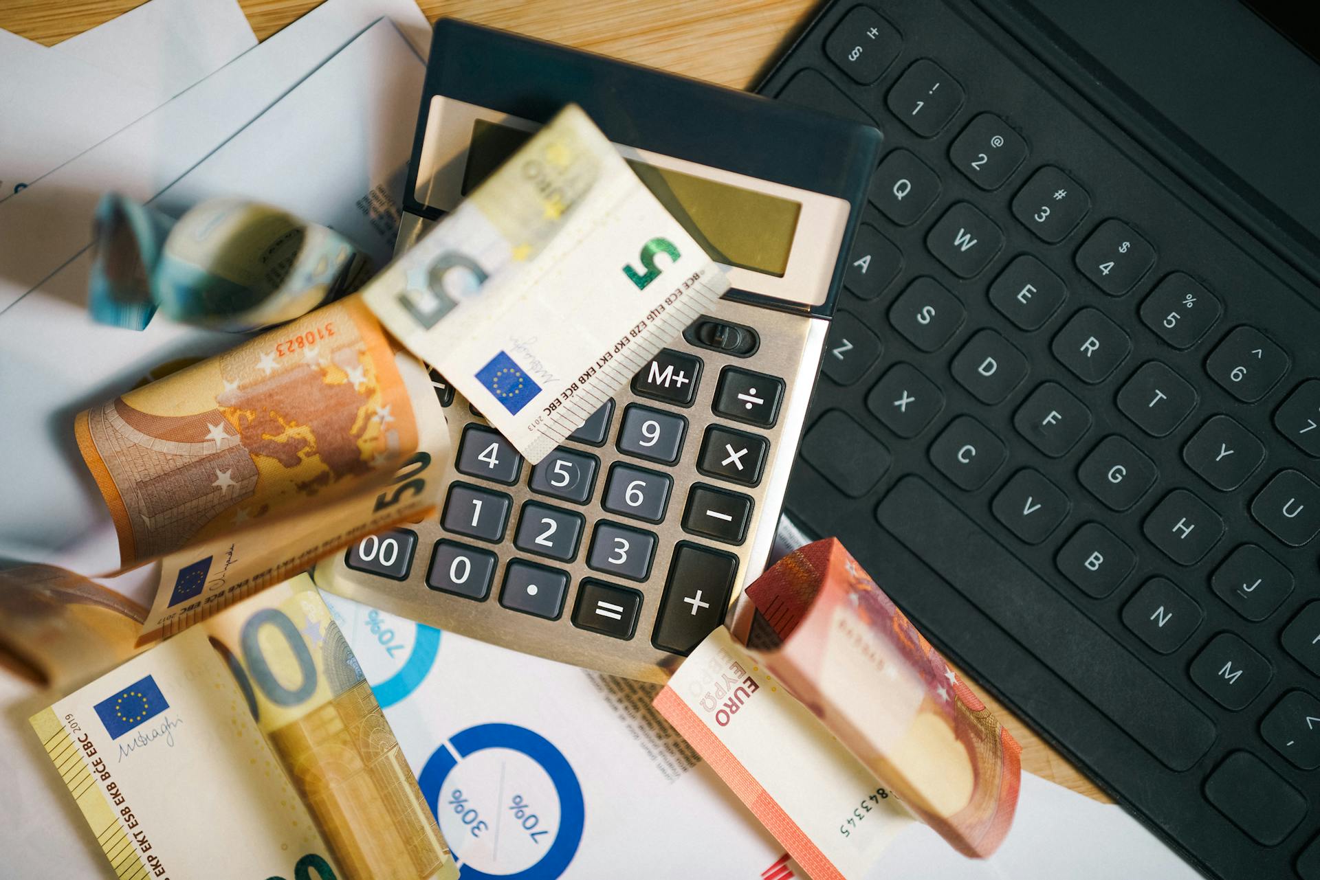 A financial setup featuring euro banknotes, a calculator, and a laptop keyboard for business analysis.