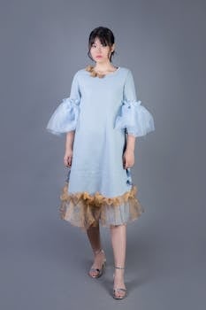 A stylish woman models a blue dress with gold accents and ruffled sleeves, perfect for a classy event.