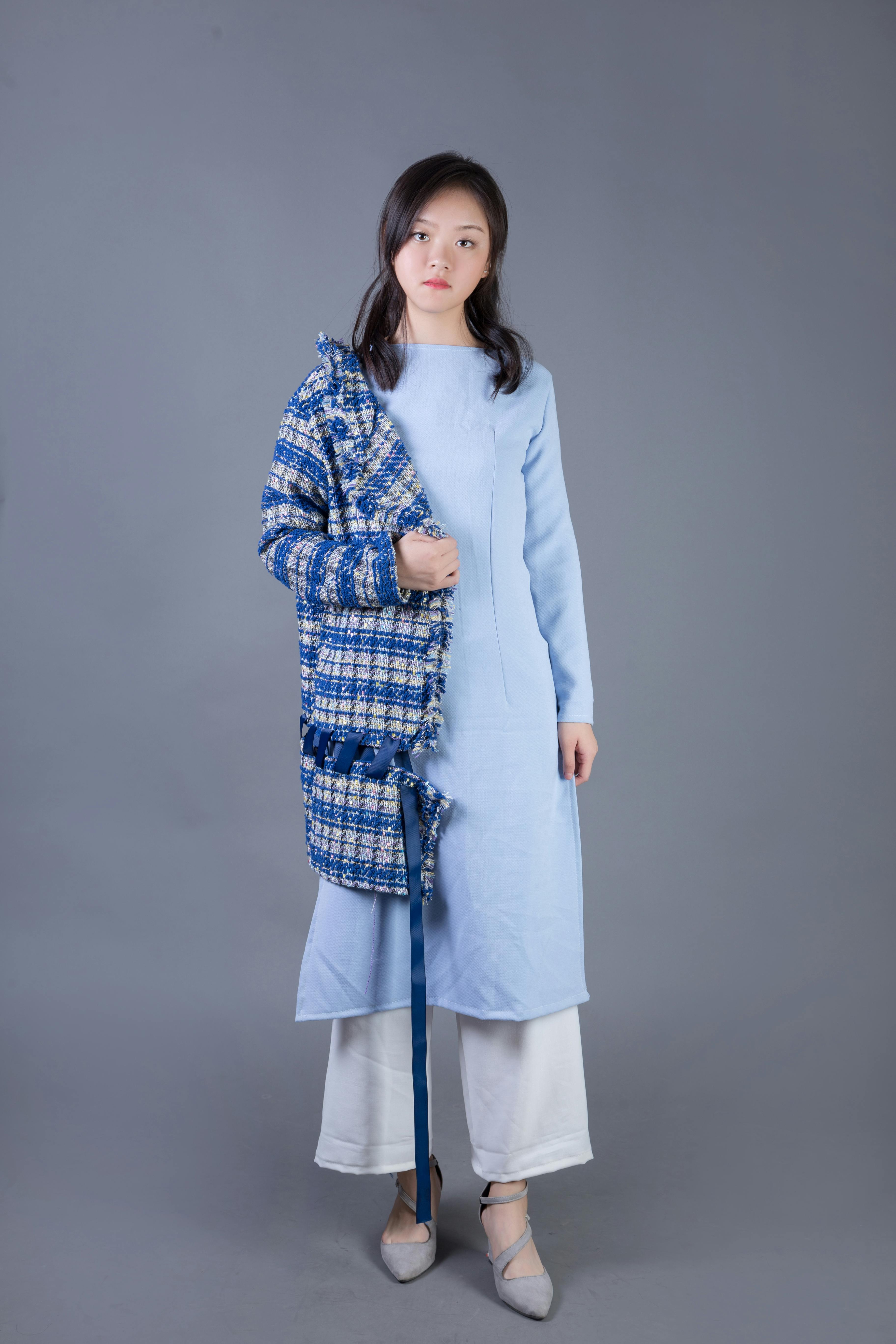 Fashion portrait of a woman in a chic blue coat and dress against a neutral background.