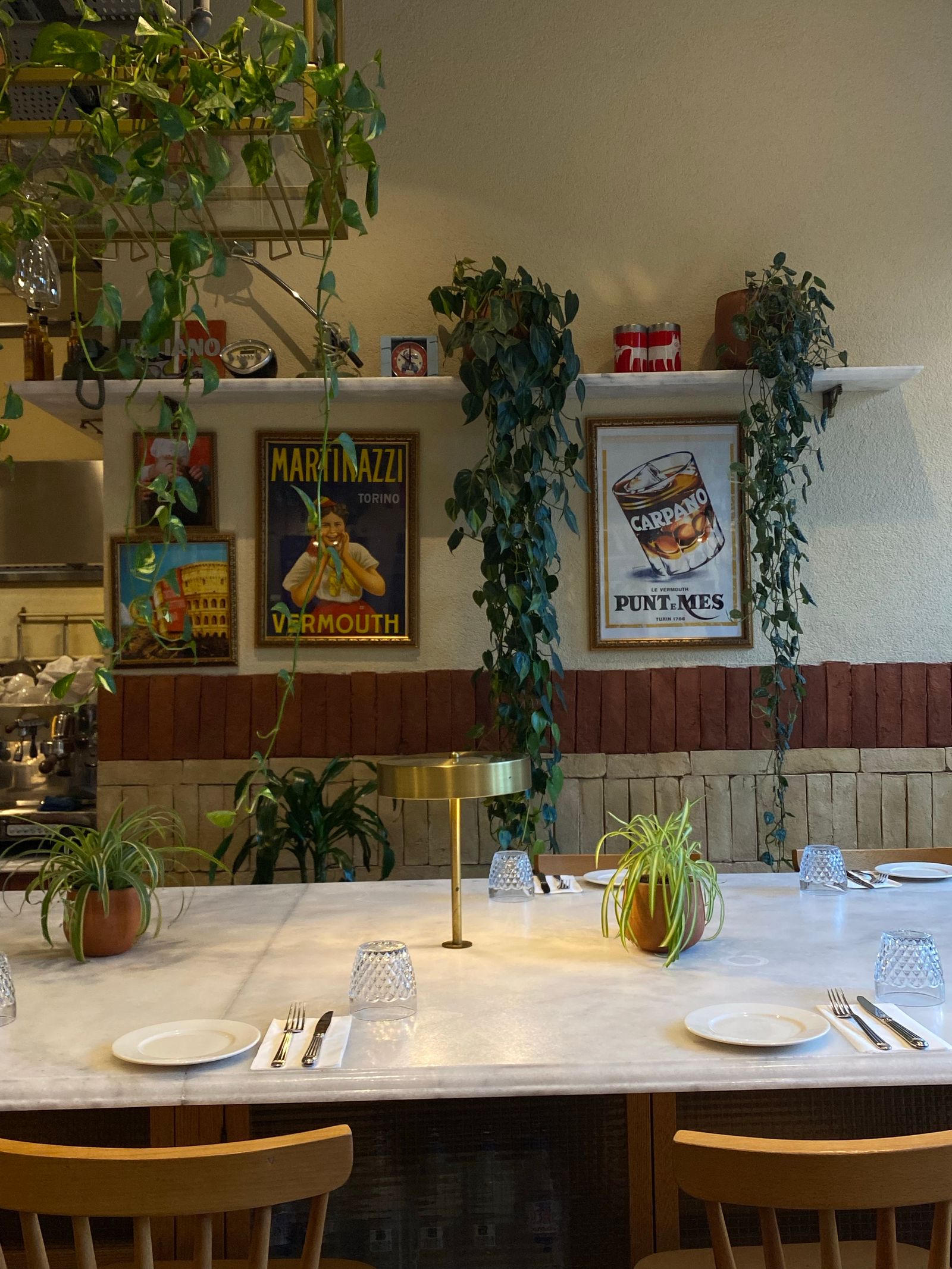 Marmortisch mit Gläsern und Pflanzen vor einer Wand mit italienischen Vintage-Plakaten