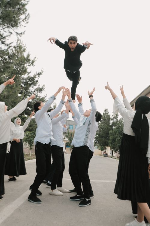 Free Joyous group of young adults throwing a friend in the air during a celebration outdoors. Stock Photo