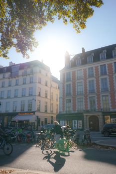 A vibrant urban street scene with bicycles parked under sunlit European architecture and people nearby.