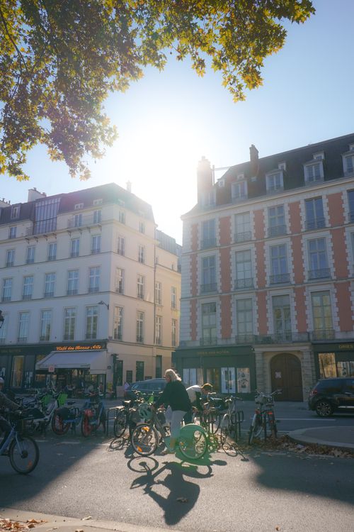 Free A vibrant urban street scene with bicycles parked under sunlit European architecture and people nearby. Stock Photo