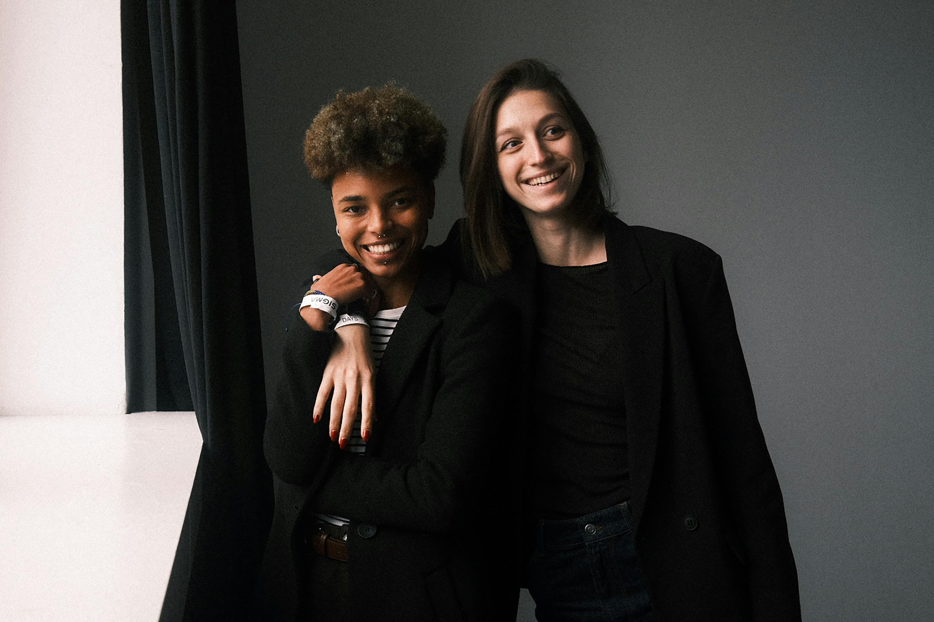 Two friends smiling and casually posing indoors, conveying friendship and happiness.