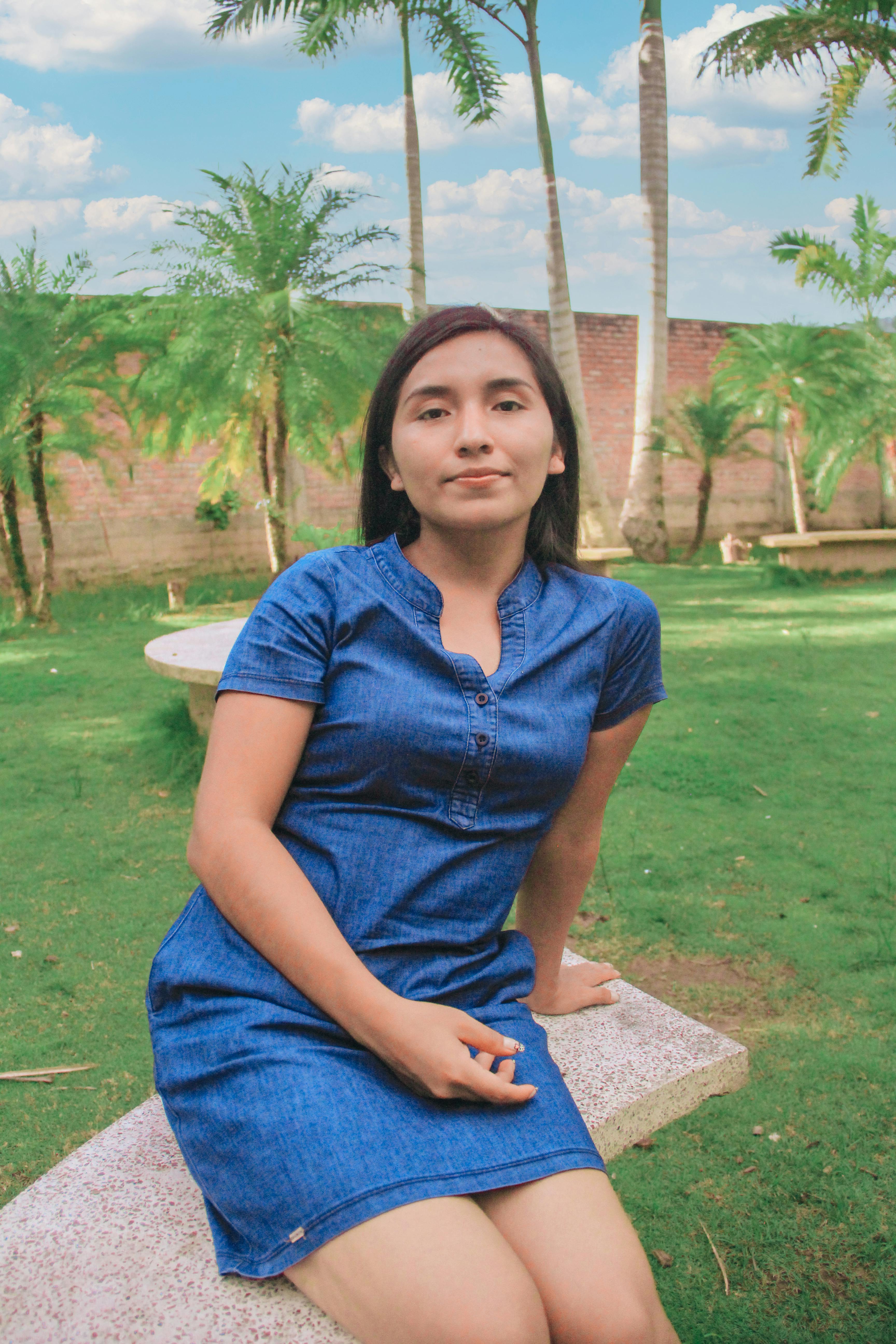Young woman in a blue dress sitting on a bench in a sunny garden.