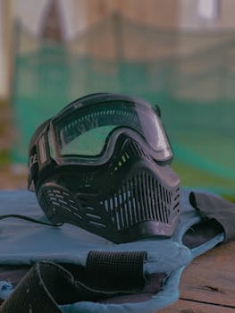 Black paintball mask on table at outdoor paintball field, ready for action.