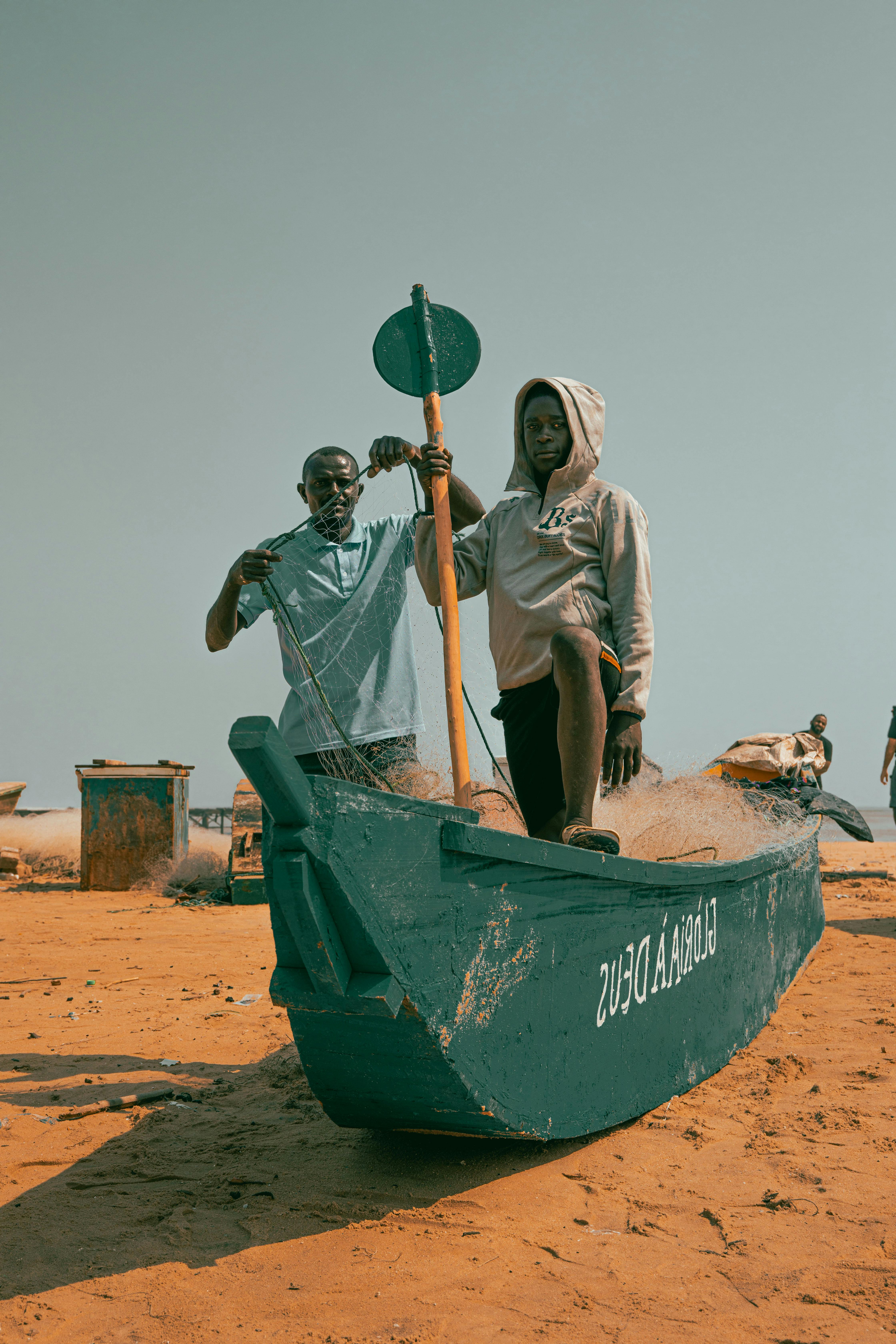 Two fishermen preparing a boat on the sandy beach of Cabinda, Angola.