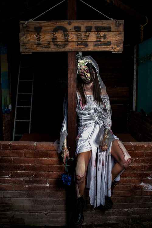 Free A costumed zombie bride sits beneath a wooden 'LOVE' sign in a dark interior scene. Stock Photo