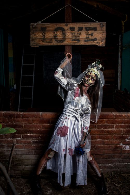 Free A zombie bride in a haunting pose beneath a rustic 'LOVE' sign. Stock Photo