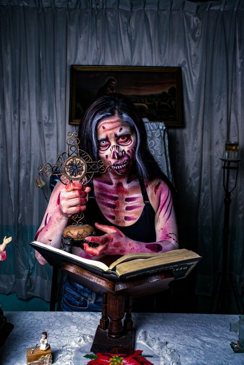Free Person in gothic skeleton makeup holding ornate cross and book in dimly lit room. Stock Photo