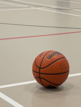 A lone basketball sits on a clean indoor court with precise white lines.
