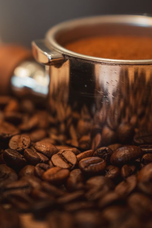 Free Rich coffee beans surrounding a stainless steel espresso pot, creating a warm and inviting scene. Stock Photo