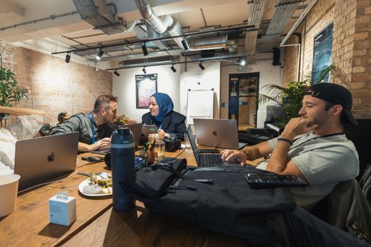 Casual office meeting with diverse team using laptops and technology in a modern workspace.