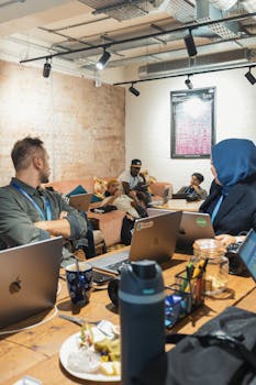 A relaxed office meeting with young adults discussing around a table with laptops.