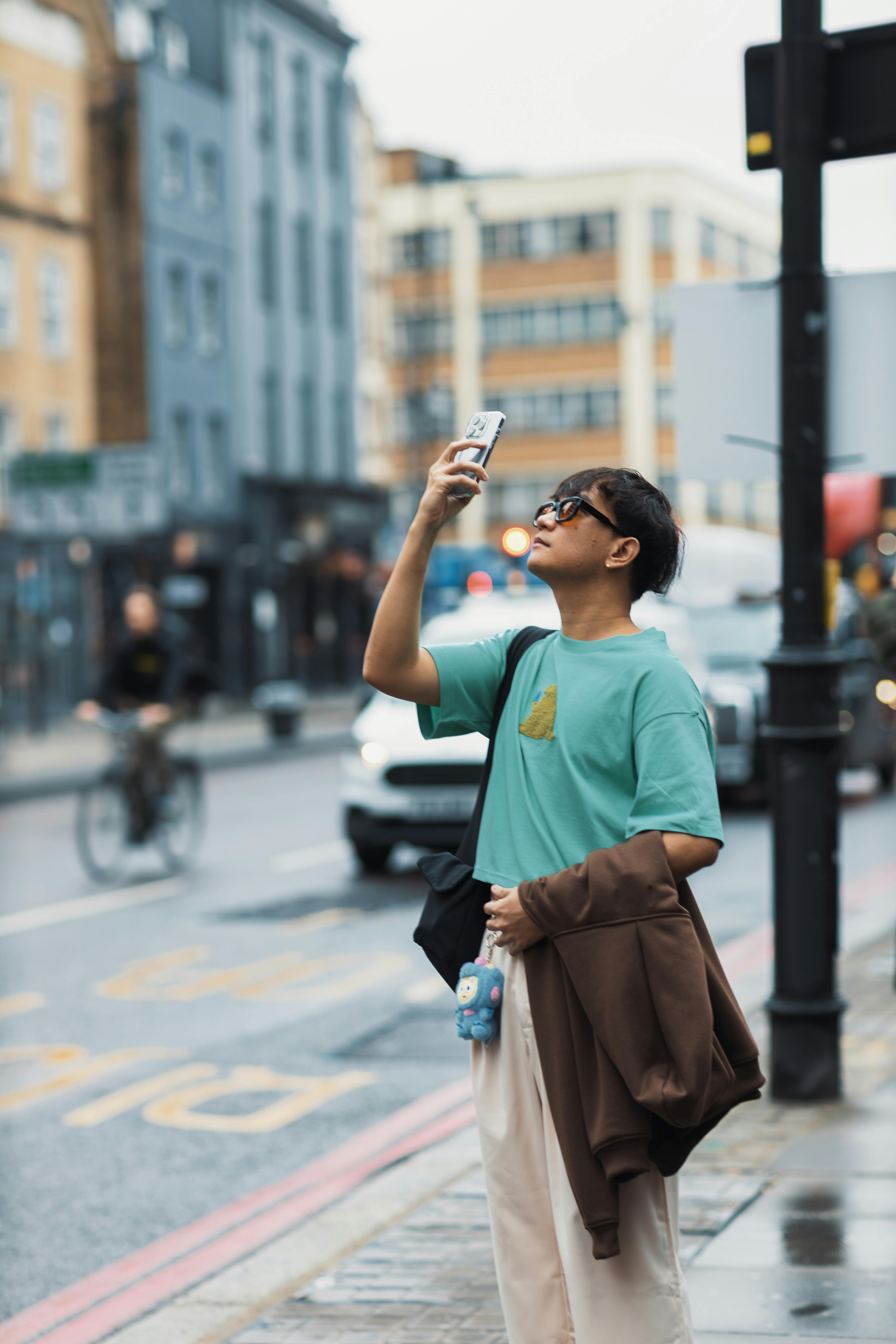 A young man captures urban scenes with his smartphone on a bustling city street.