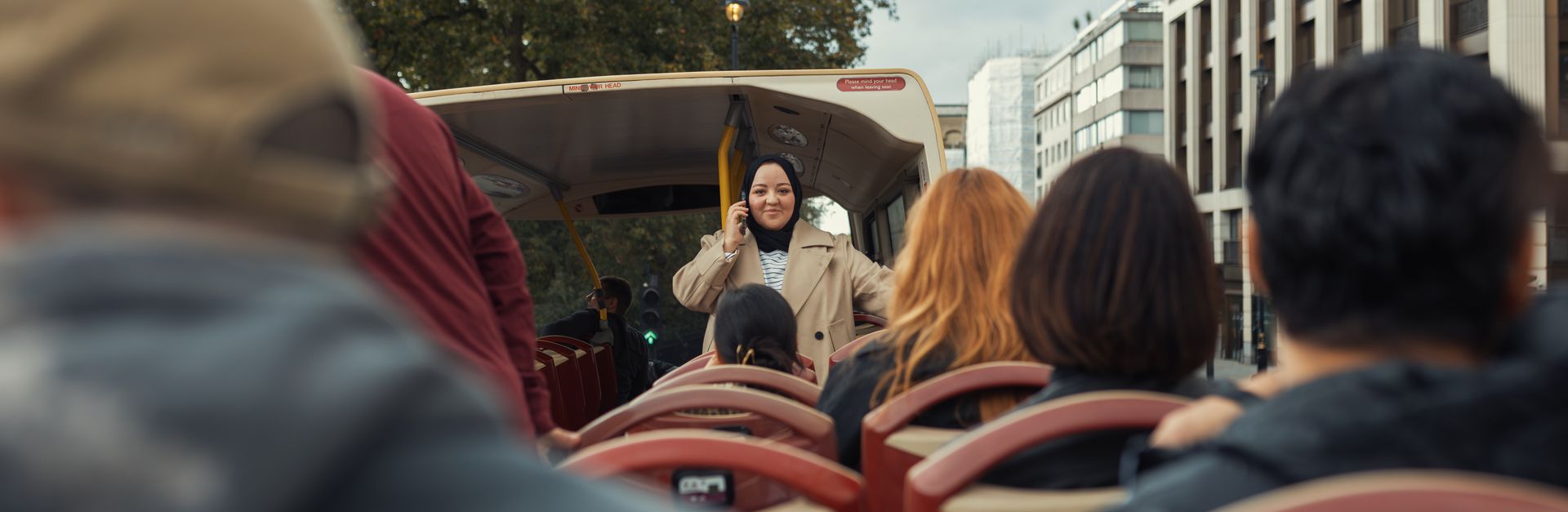 A diverse group of people enjoys a city tour on an open-top bus surrounded by urban architecture and