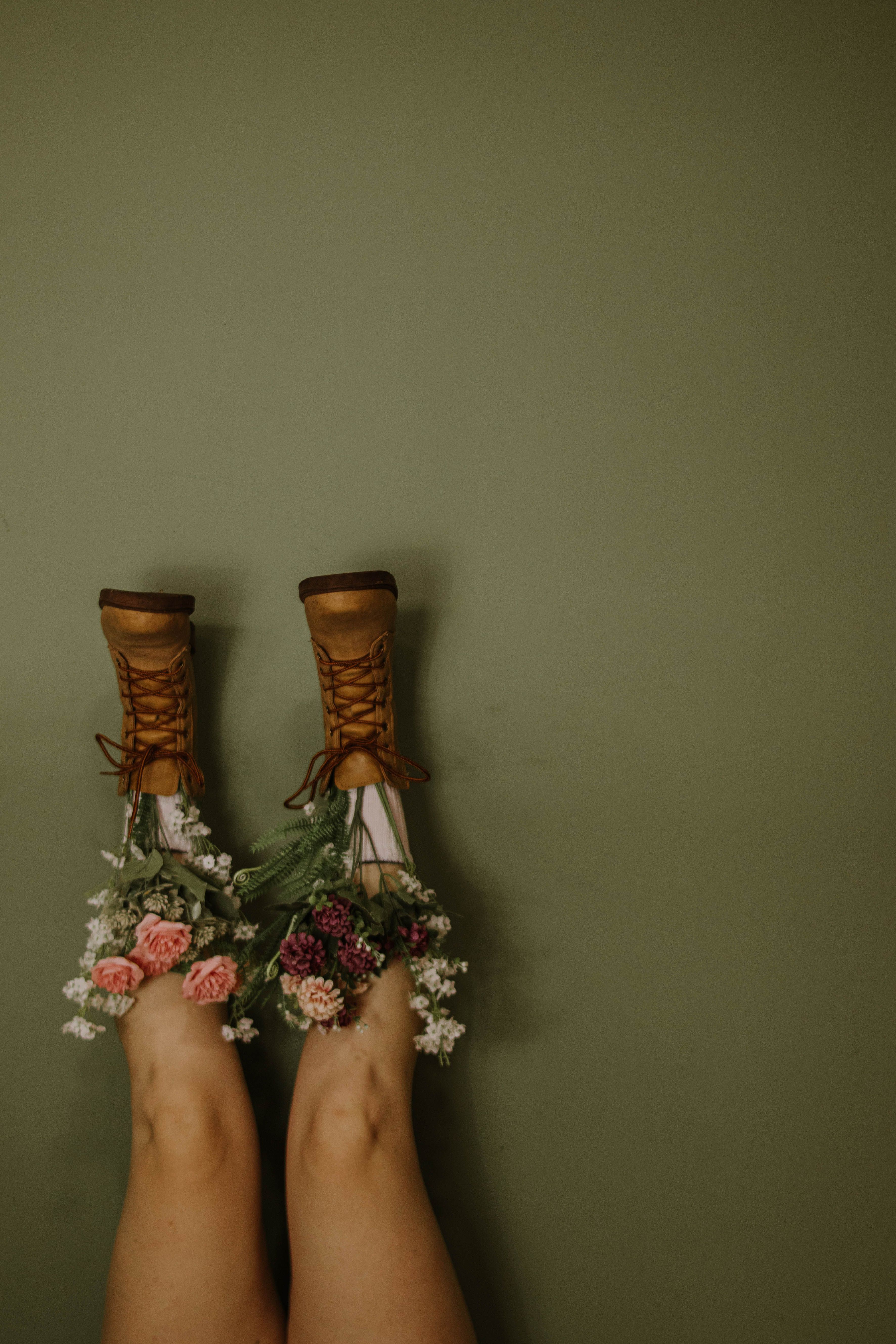 Playful composition of boots overflowing with flowers against an olive green backdrop.