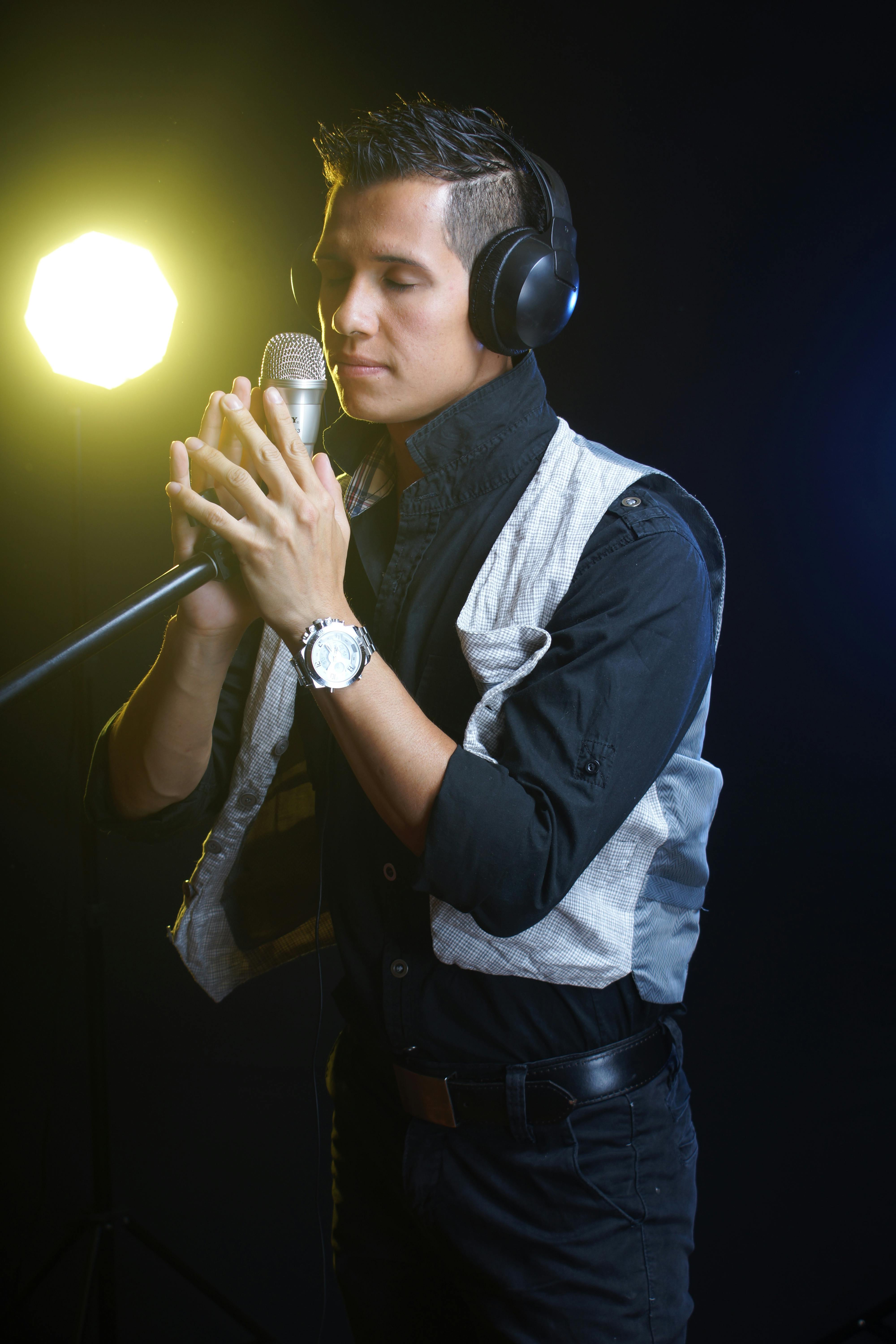 Young male singer in studio with headphones and microphone, focused and expressive.