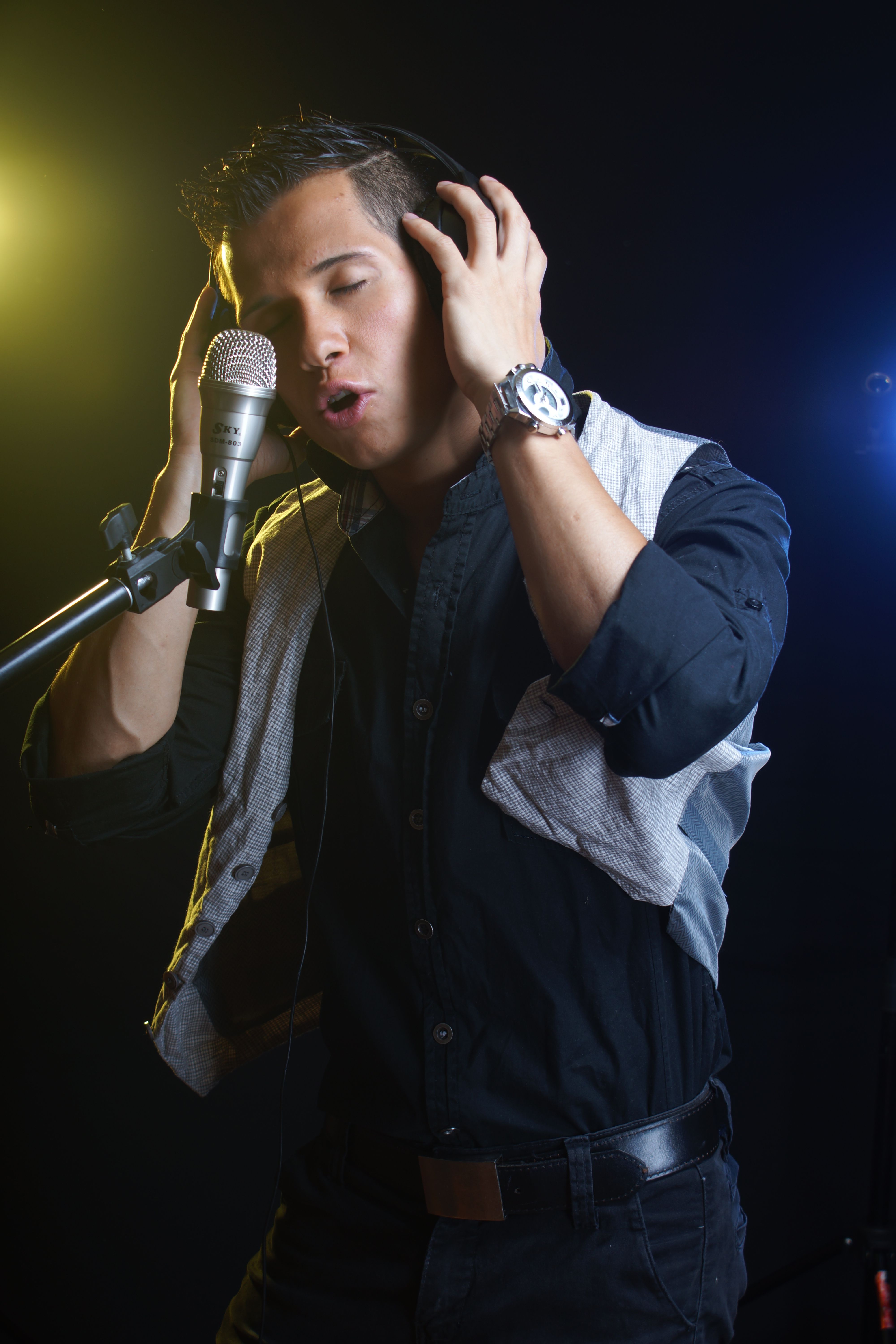 A young man passionately singing into a studio microphone, wearing headphones.