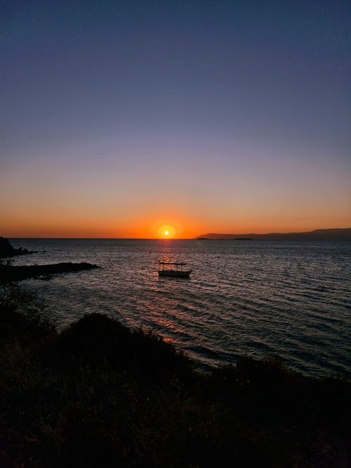 Free A peaceful sunset view with a silhouette of a boat on calm waters, creating a tranquil atmosphere. Stock Photo