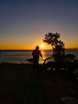 Silhouette of a person by the ocean during a picturesque sunset.