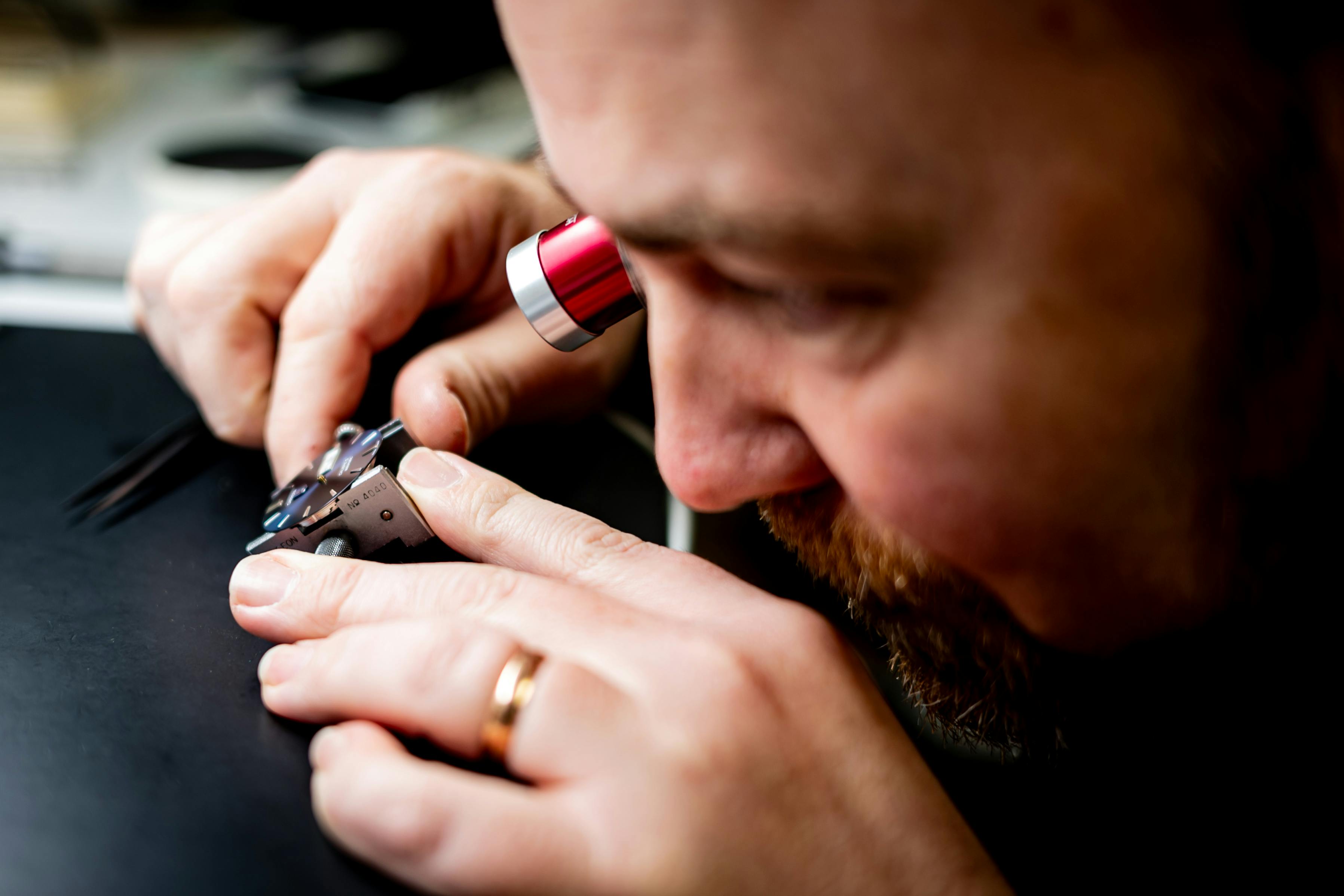 Skilled watchmaker uses magnifying glass to adjust intricate watch components with precision tools.