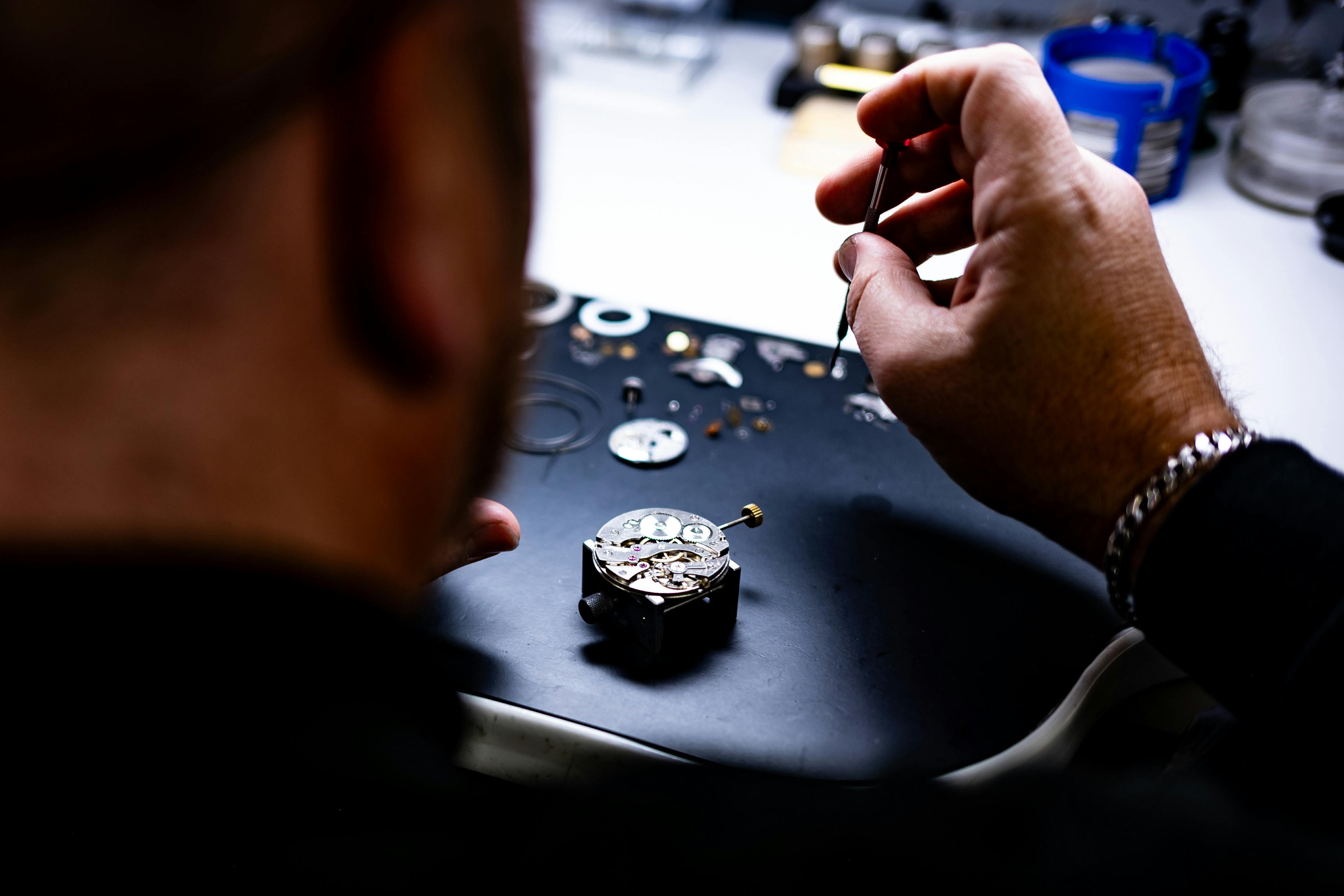 Watchmaker meticulously assembling a watch with precision tools on a workbench.