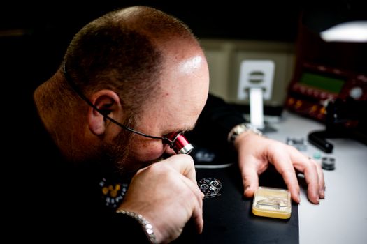 Skilled artisan closely inspects a watch mechanism using magnifying glass for precision