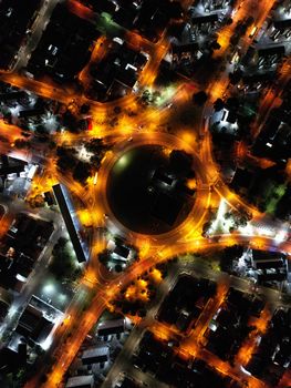 Brightly illuminated city roundabout captured from above at night.