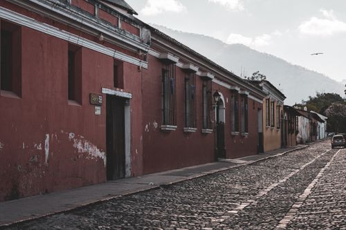 Free Cobblestone street in Antigua Guatemala lined with colorful colonial buildings and mountains in the background. Stock Photo