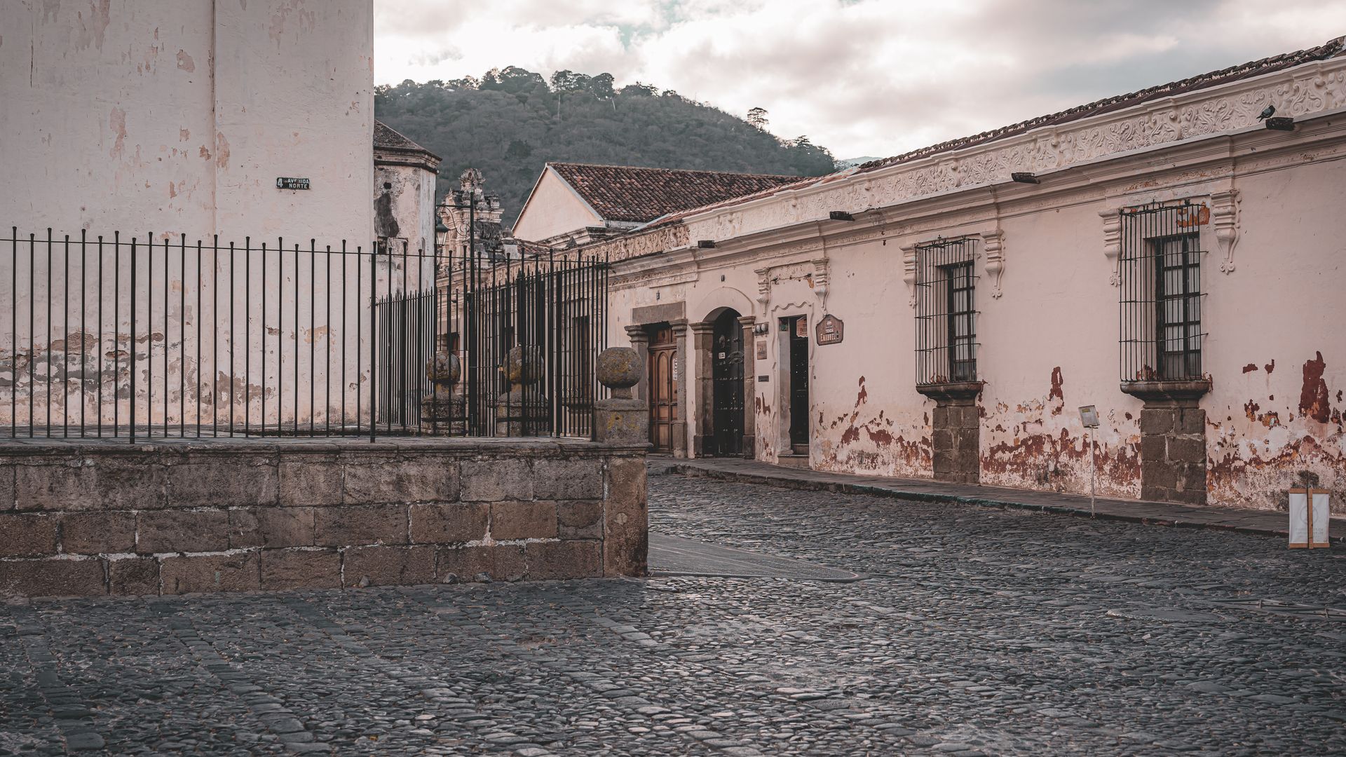 A cobbled colonial street of low houses with hills behind