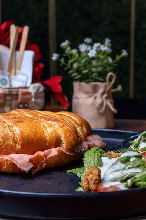 Free Tasty croissant sandwich with prosciutto and fresh salad on a plate. Stock Photo