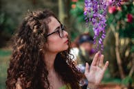 阳光明媚的日子里，一位卷发女子在公园里侧身观赏紫色的紫藤花