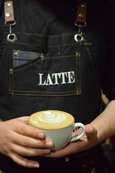 Barista in apron holding a cup with beautiful latte art design, perfect for coffee lovers.