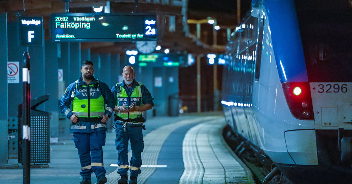 Security personnel patrol Jönköping train station at night with a blue train nearby.