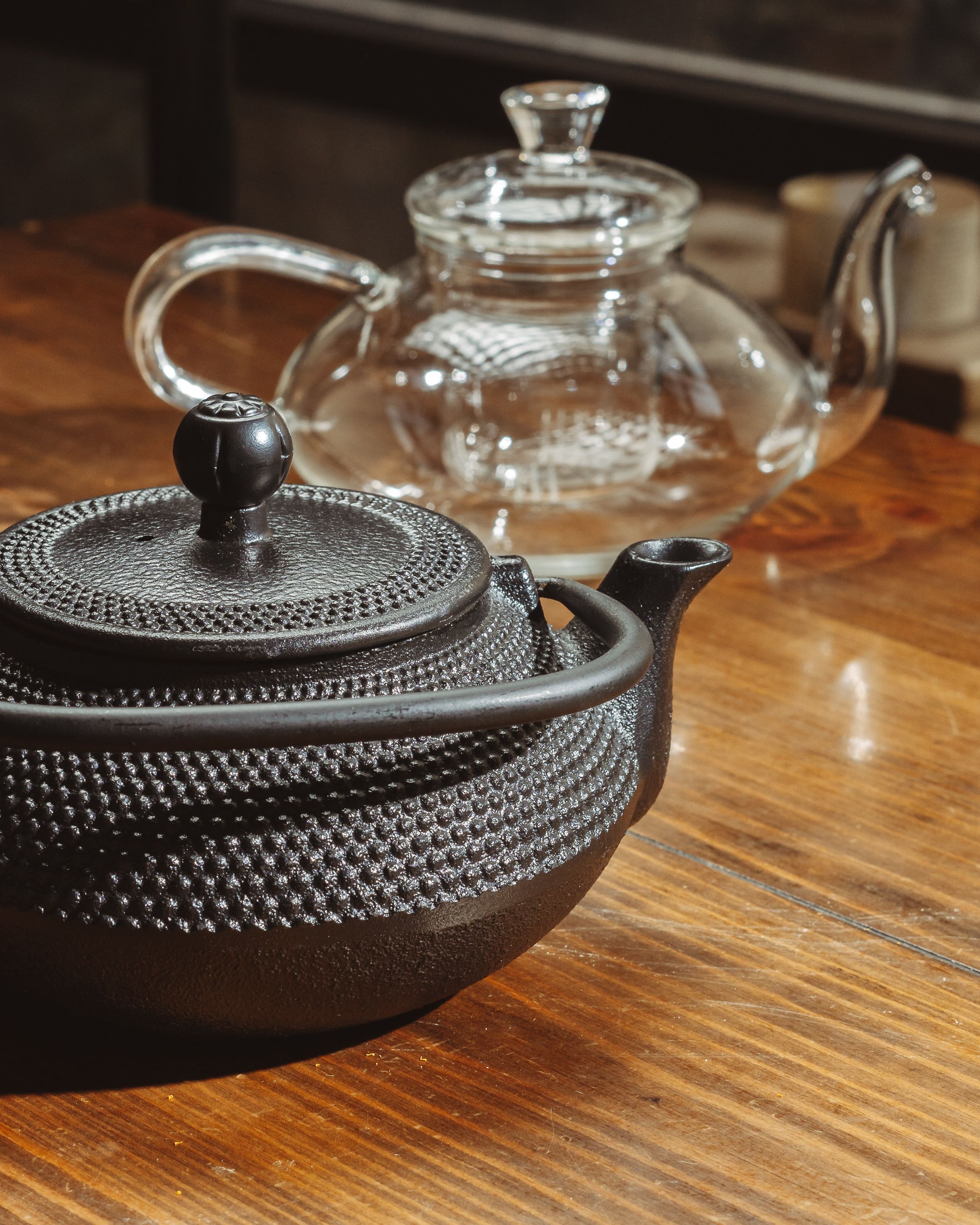 Cast iron and glass teapots on sunlit wooden table