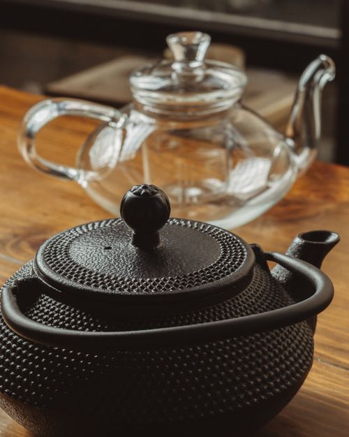 Free A black cast iron and glass teapot elegantly arranged on a wooden table, reflecting a warm and cozy atmosphere. Stock Photo