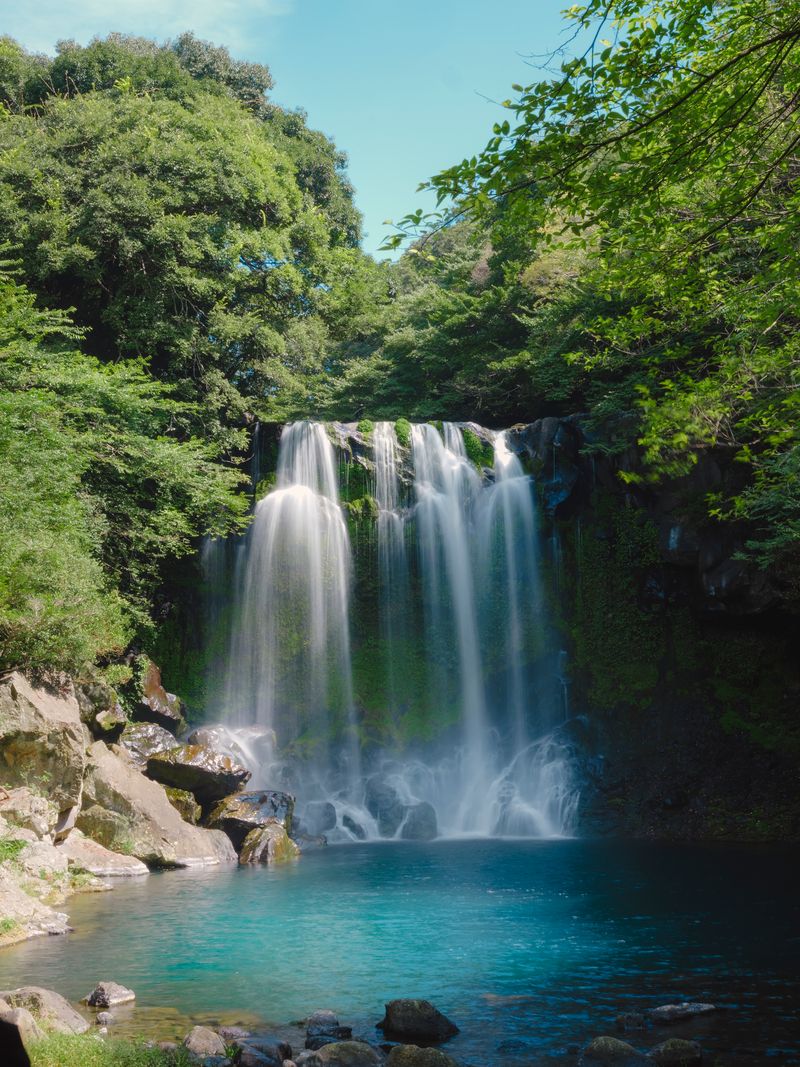 Cheonjeyeon Falls pouring over mossy rocks into a turquoise pool on Jeju Island