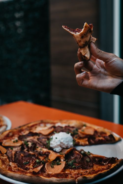 Free Close-up of a pepperoni pizza slice held by hand with pizza background. Stock Photo