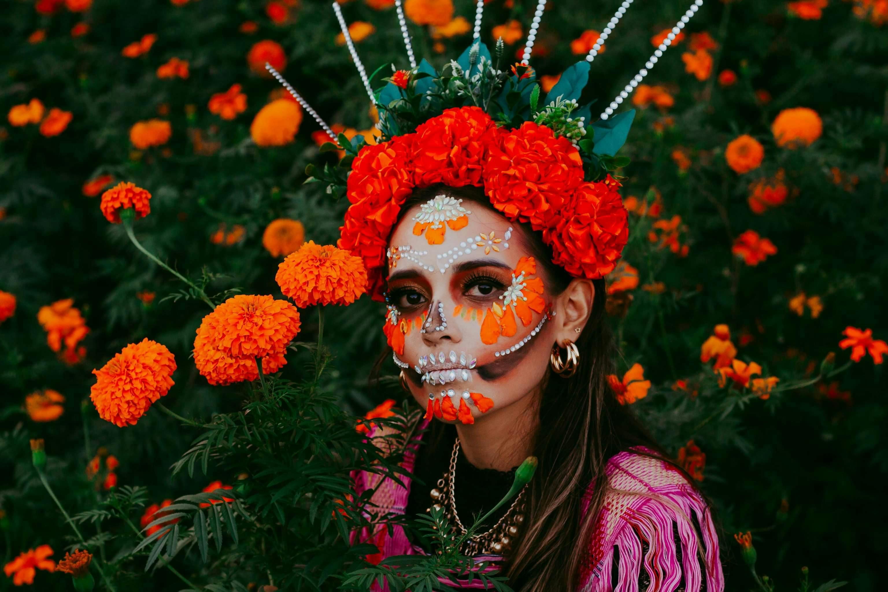 Woman with traditional Dia de los Muertos white and black sugar skull face paint surrounded by vibrant orange marigold cempasuchil flowers