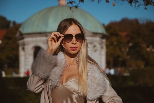 Elegant woman in sunglasses posing in Munich with an iconic garden backdrop.