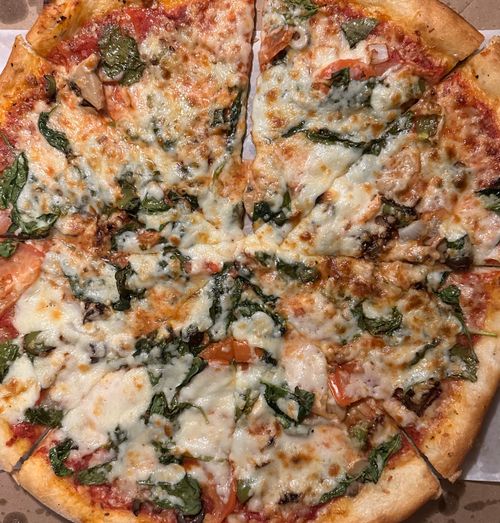 Free Close-up of a cheesy vegetarian pizza with fresh spinach and tomatoes. Stock Photo