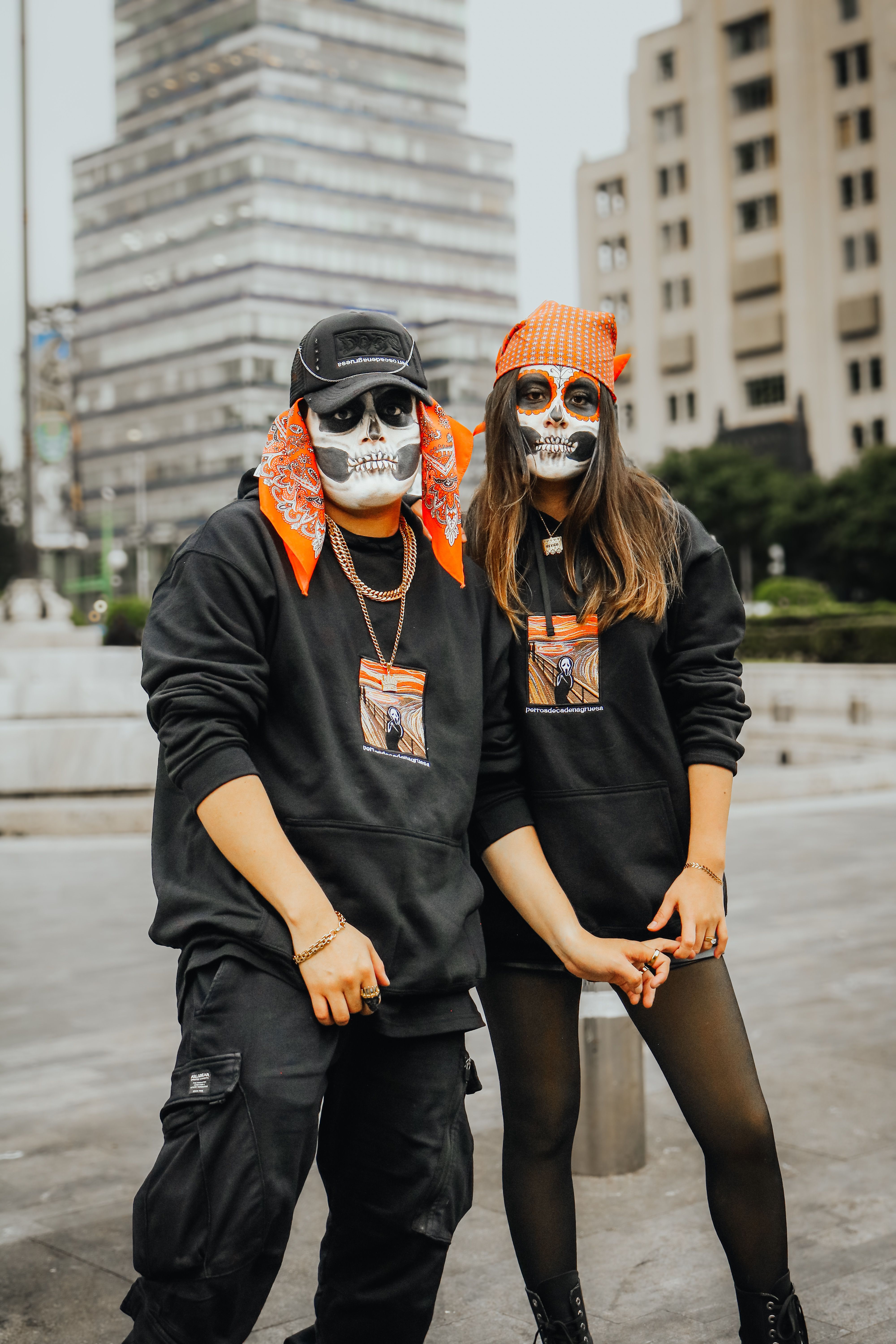 A couple in skeleton makeup poses outdoors in an urban setting.