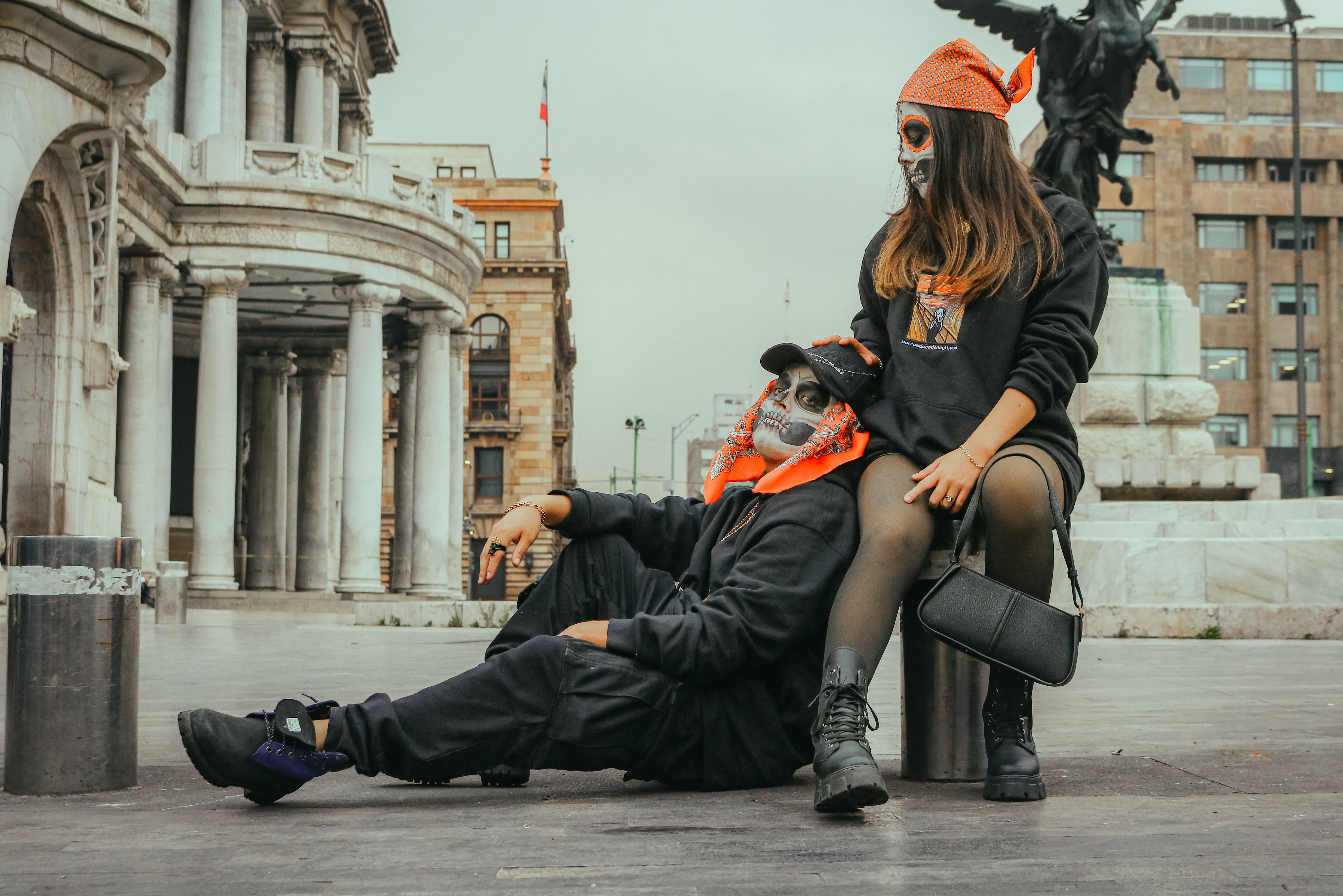 Two young adults with artistic face paint in a cityscape near a historic building.