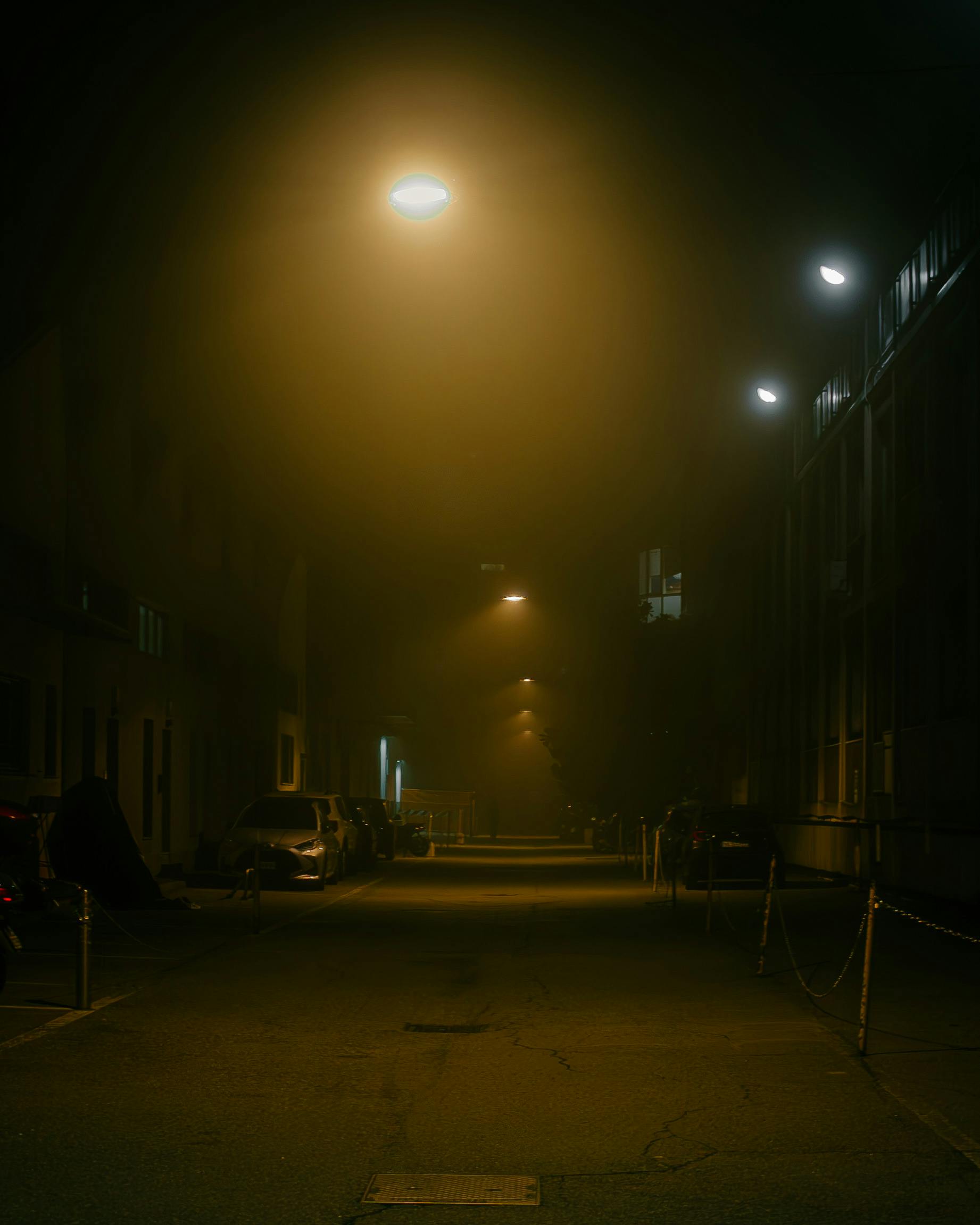 A mysterious foggy street at night in Milano, Italy, lit by warm streetlights.