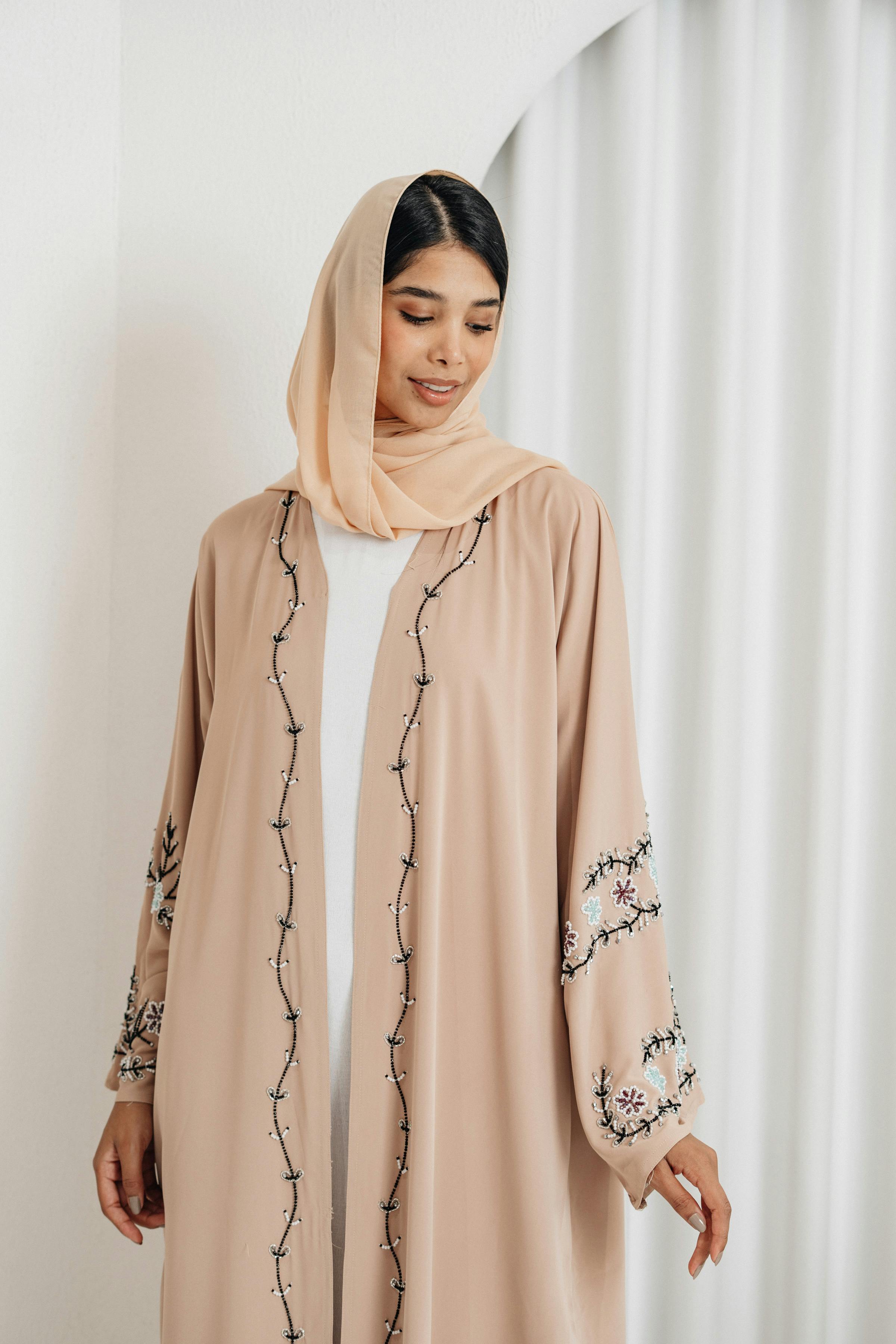 Portrait of a woman wearing an embroidered beige abaya in a serene indoor setting.
