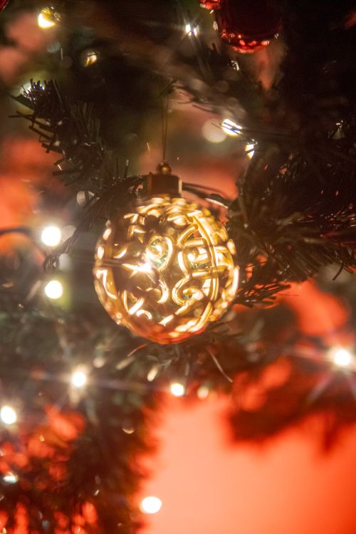 Free Warm glowing Christmas ornament on a tree with festive lights, creating a cozy holiday ambiance. Stock Photo